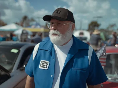 Retrato documental de un hombre de barba blanca en una exhibición de autos clásicos al aire libre