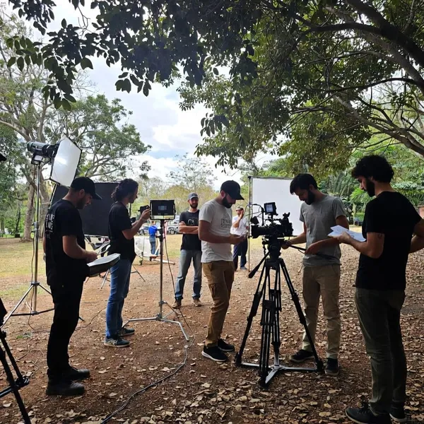 Equipo de filmación preparando cámara y luces al aire libre bajo los árboles